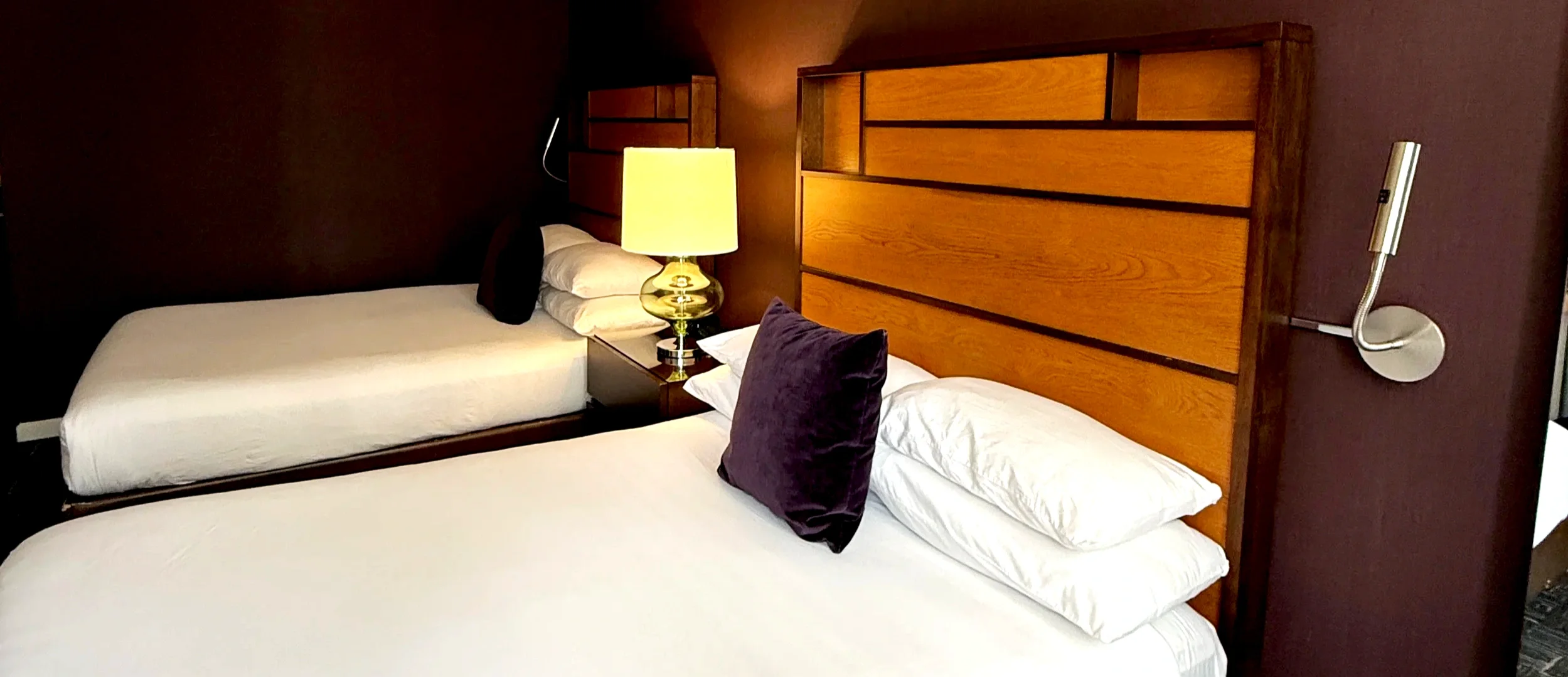 Two white hotel beds against wooden headboards with a bedside lamp