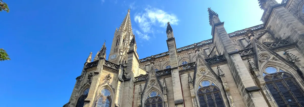 Gothic cathedral facade with a tall stone spire under blue sky