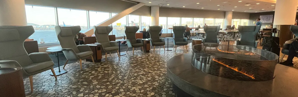 Airport lounge with gray wing chairs around a circular fireplace