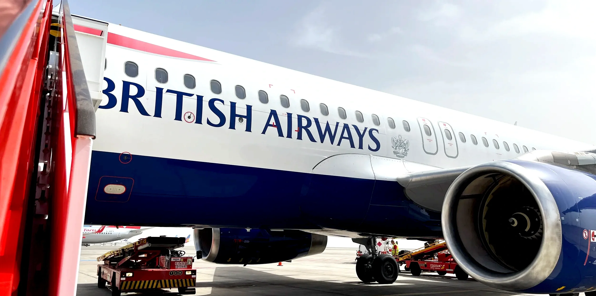 British Airways jet at the gate beside a red jet bridge